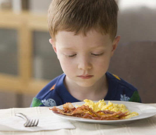 Caucasian boy looking at plate of eggs and bacon. Concept image for fussy eaters.
